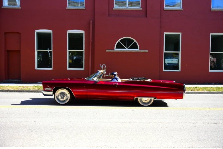 a woman drives an old style red convertible car