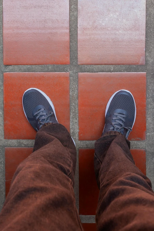 someone in a brown pair of pants standing on a red and gray tile floor