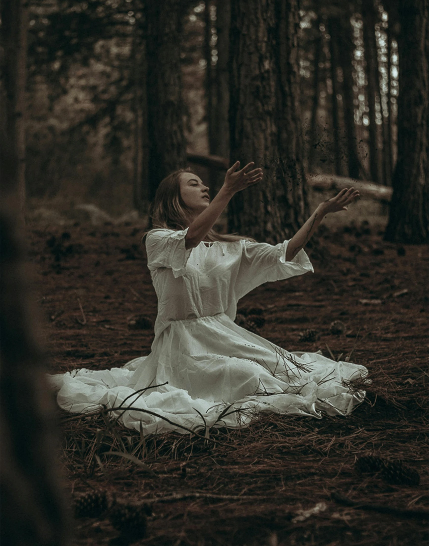 a woman in white sitting on the ground in the woods