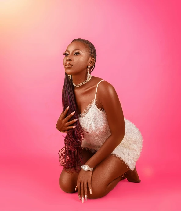 a woman kneeling down on a pink background wearing a white dress