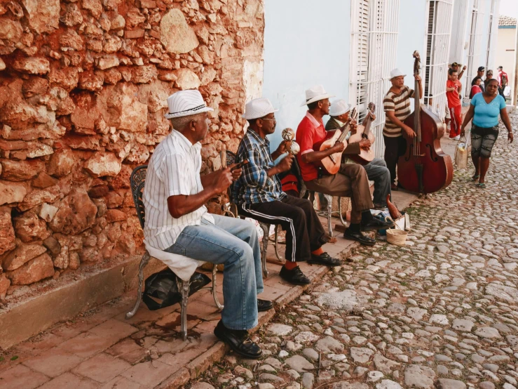 men in old fashioned attire sit on chairs while one plays the guitar