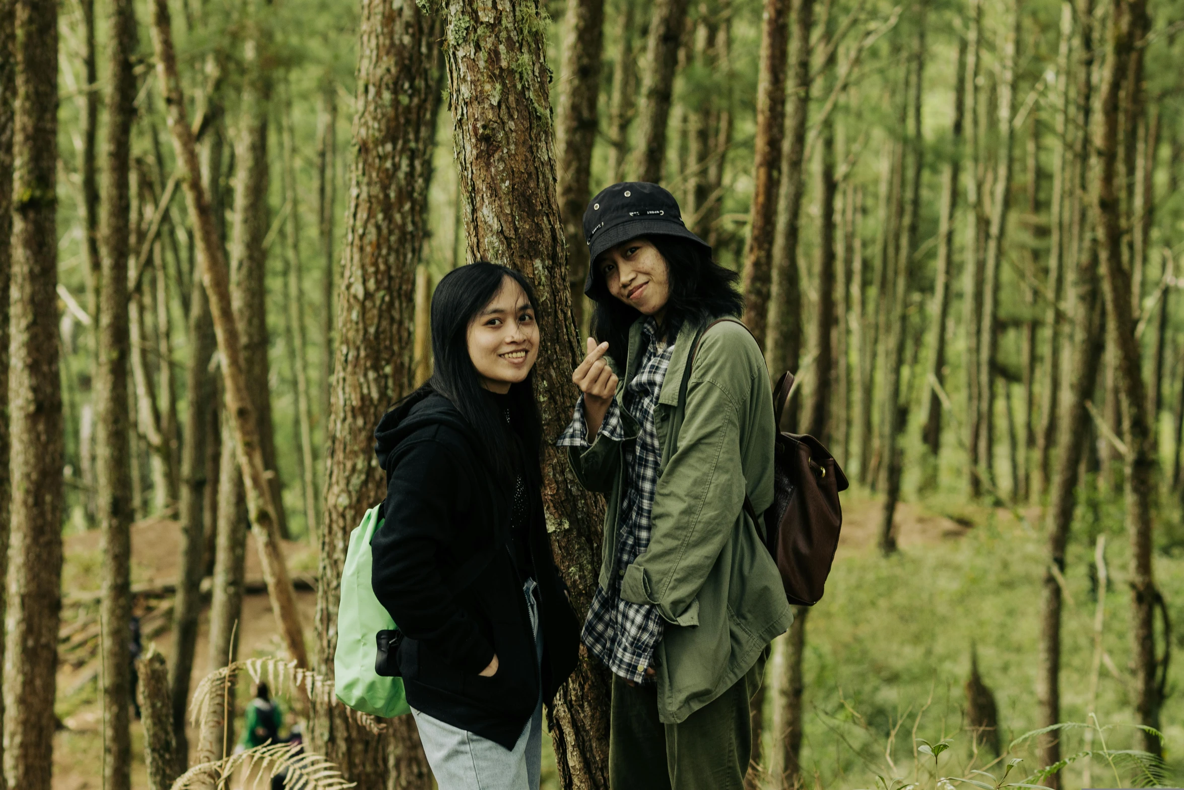 two women stand by a tree in a forest