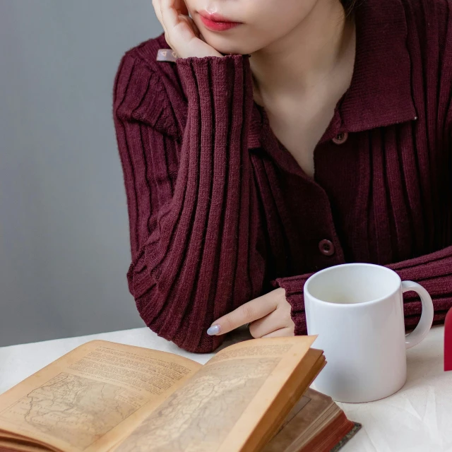 a woman sits with a book and teacup