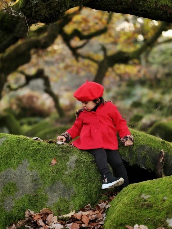 a small child sitting on top of some rocks covered in green moss