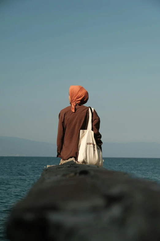 a man in orange headgear sitting at the beach looking out