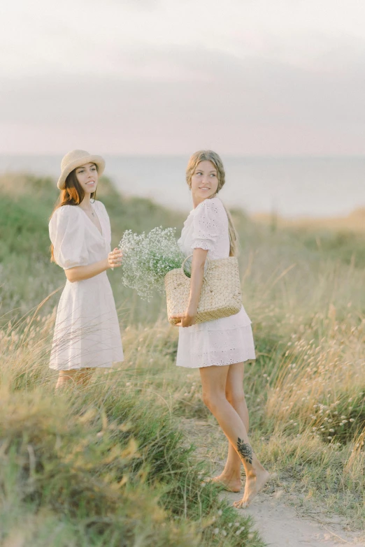 two women stand on the sand in dress and hats