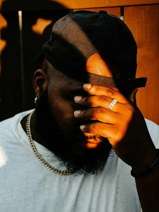 a man wearing a white shirt and wearing a black hat is covering his face with a chain