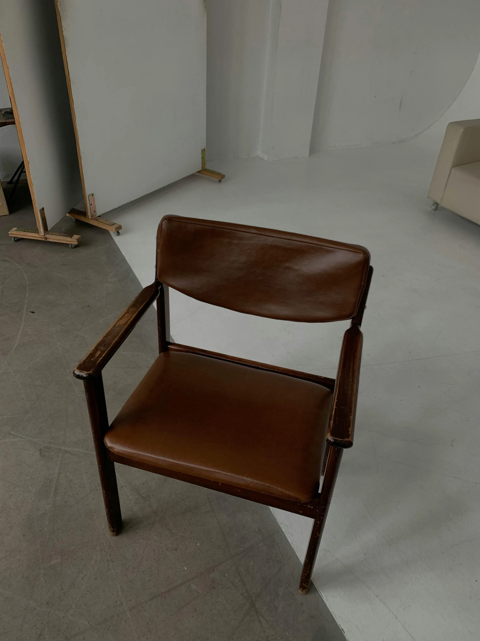 a brown leather chair with a wooden arm rest in an empty room