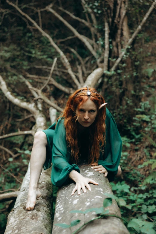 red haired girl wearing a green outfit is sitting on a log