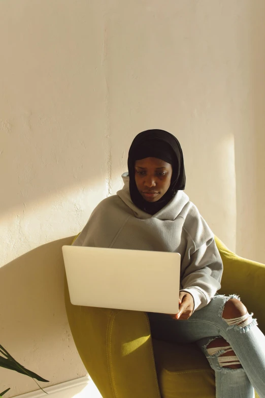 a person sits on a yellow chair with her laptop