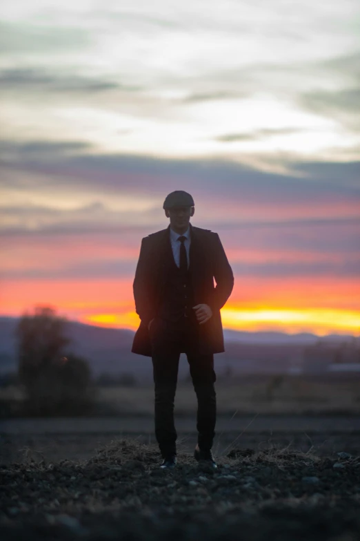 a man with his arms on his hips standing in the middle of a field at sunset