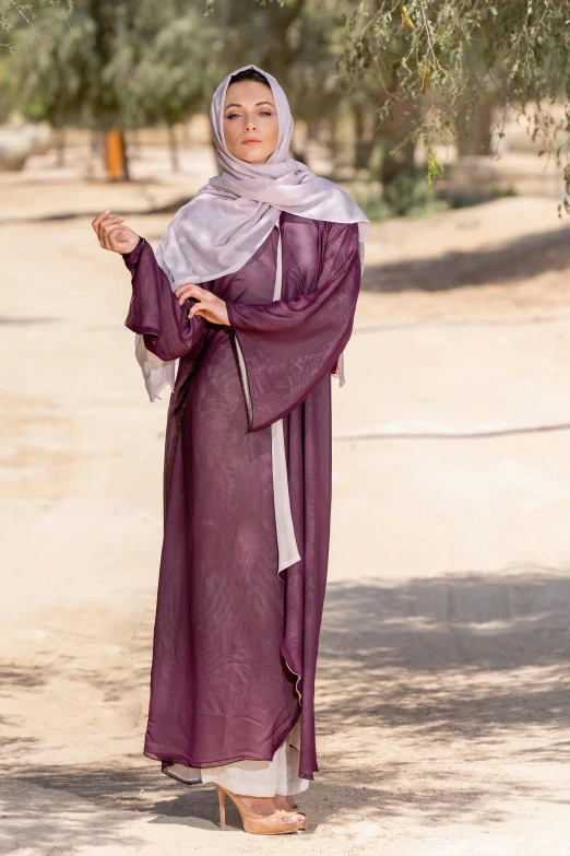 a woman standing under a tree with her hands clasped