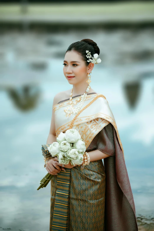 a woman holding a bouquet of flowers while standing next to water