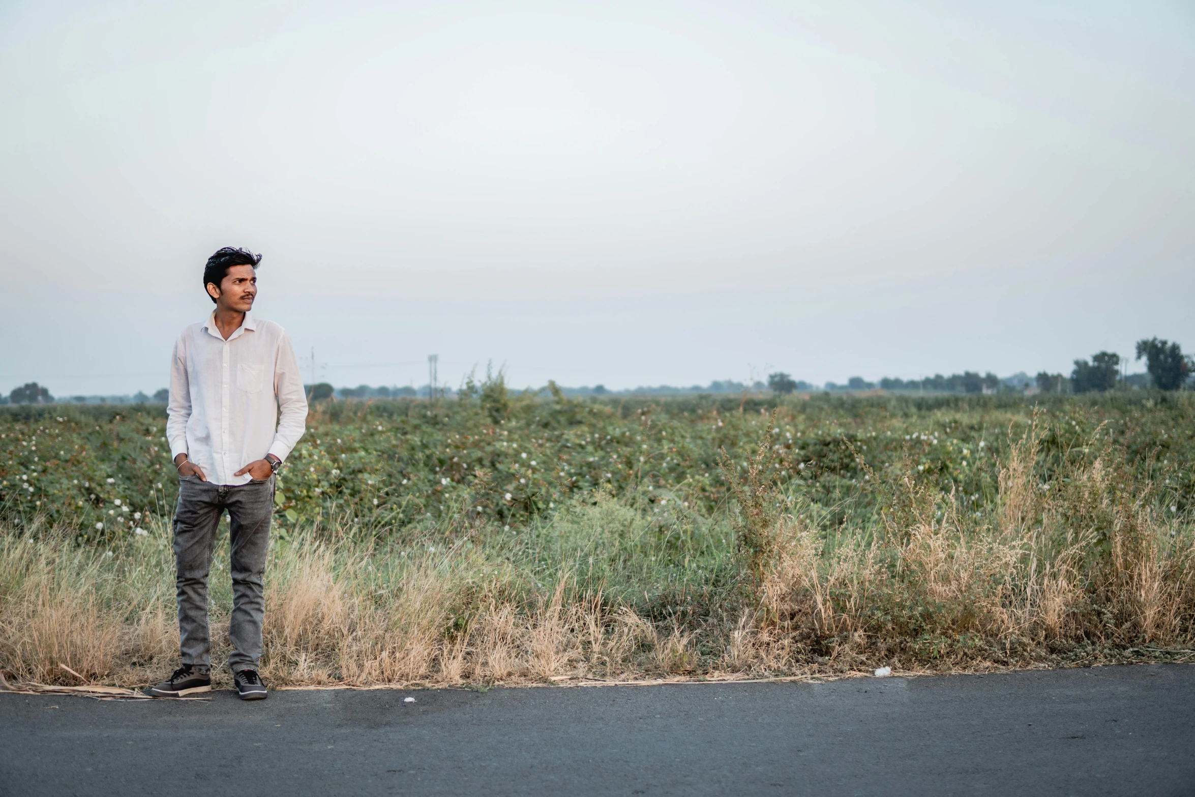 a man standing on the side of a road in a field