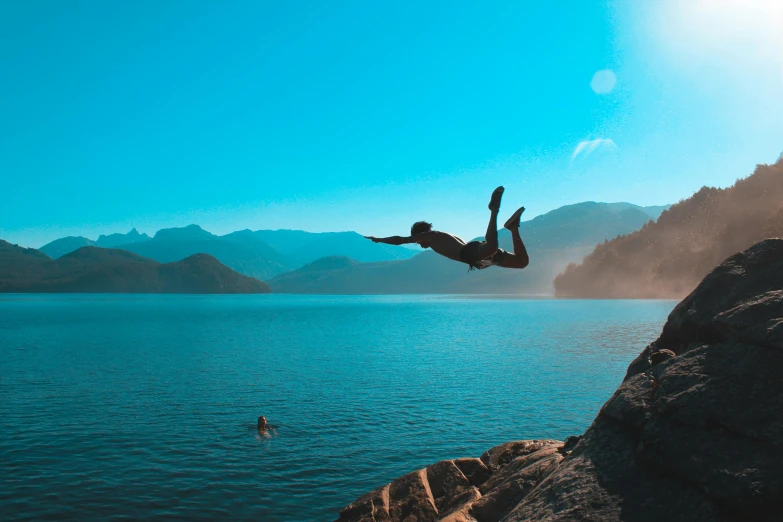 a man jumping off of a cliff into the water