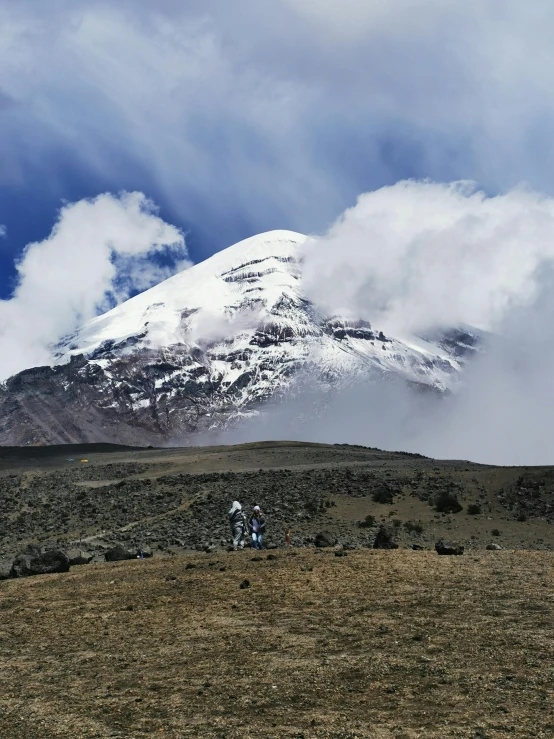 two men hiking on a grassy plain with a snow covered mountain in the background