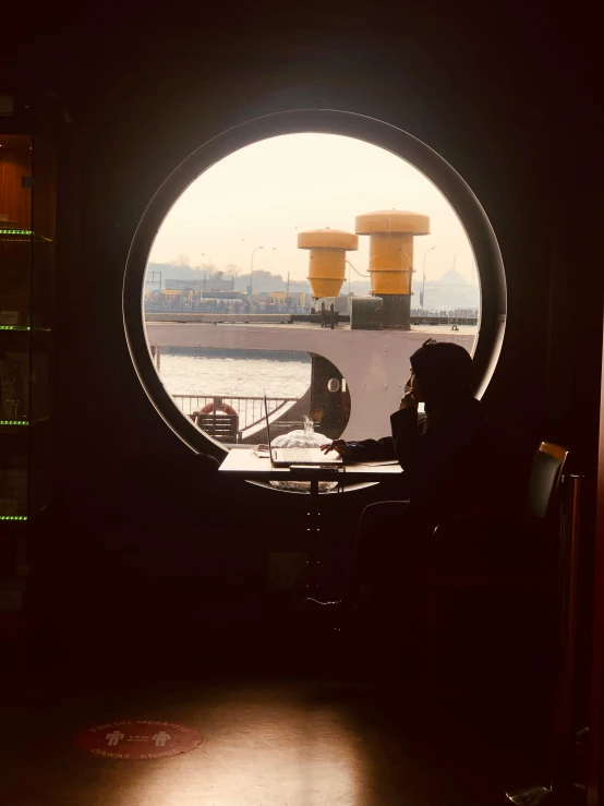 a person sitting at a table in a port looking out a window