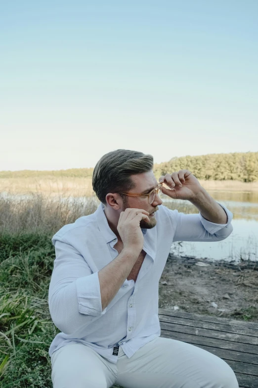 a man with glasses sitting by a lake