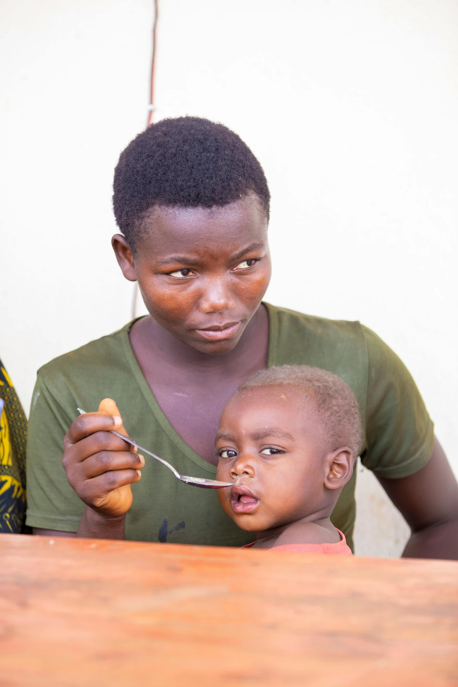 woman helping a child to feed carrots from a spoon