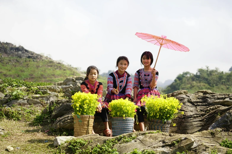 three s are sitting on the rocks holding an umbrella