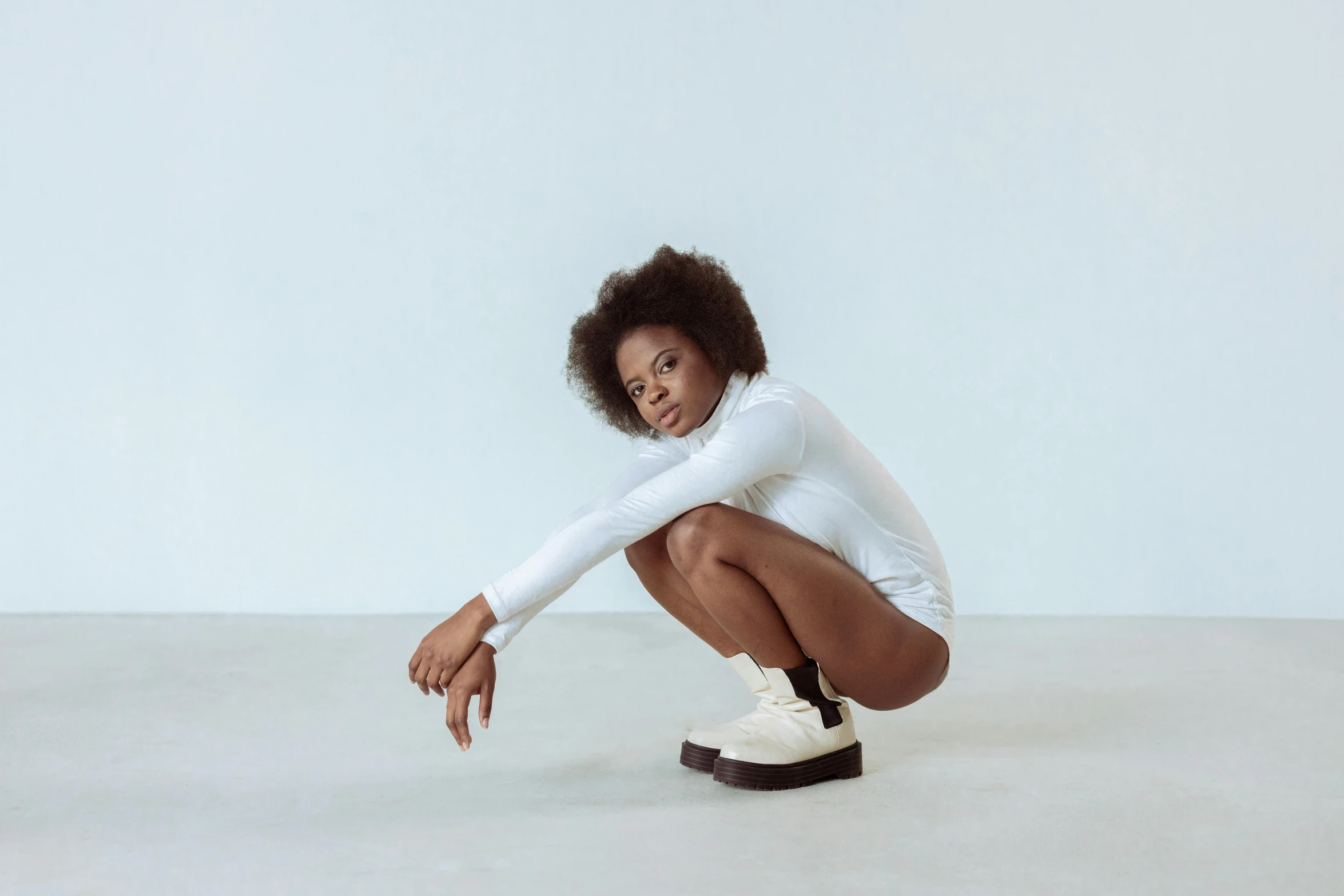 a woman crouches down wearing white shoes