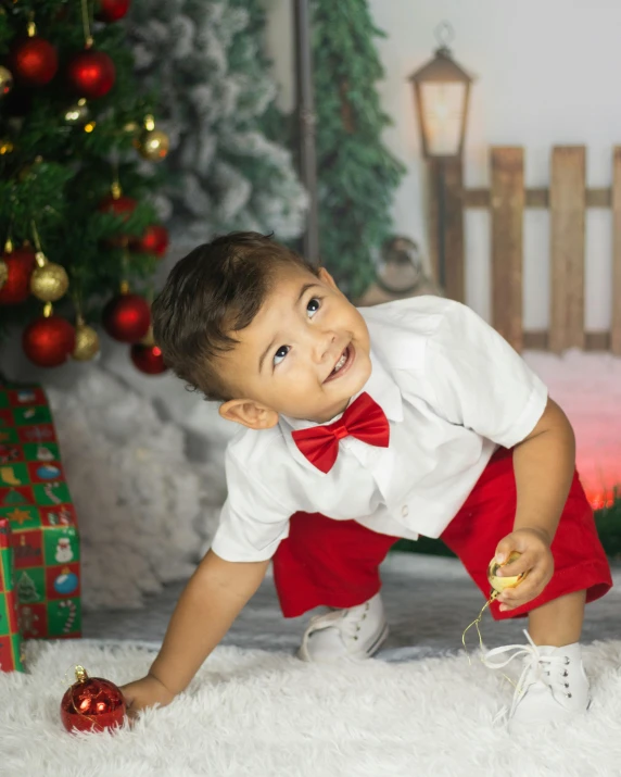 a small boy is kneeling down next to a christmas tree