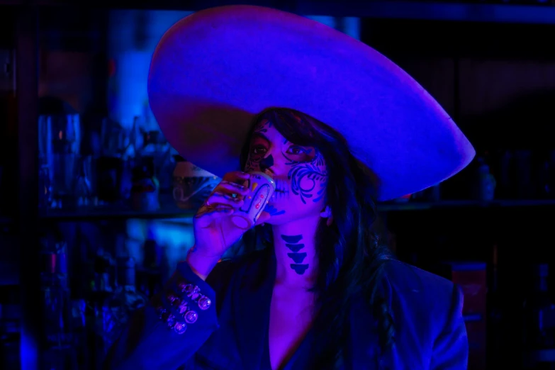 a woman with dark make up and a large hat drinking a drink