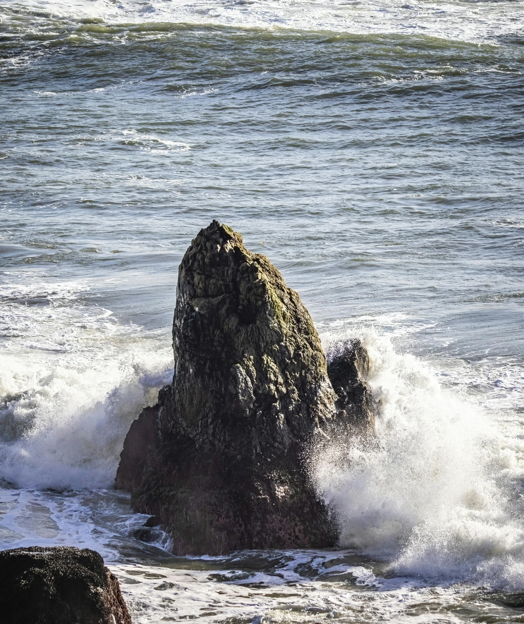 an open expanse of water with rough surf breaking up around a rock