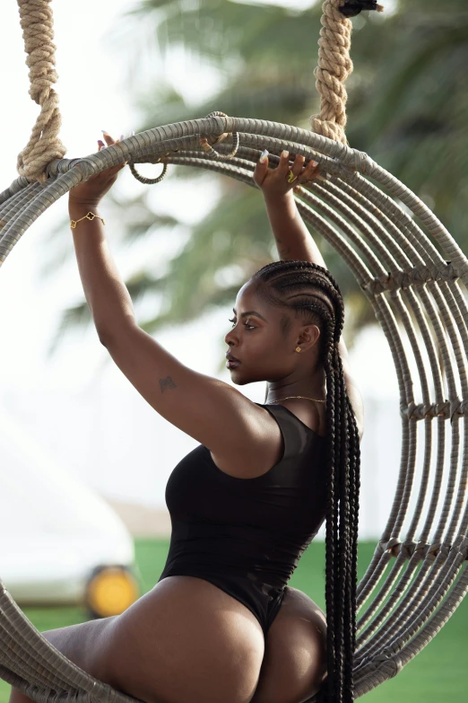 a beautiful black woman in a black bikini holding onto a round roped hammock