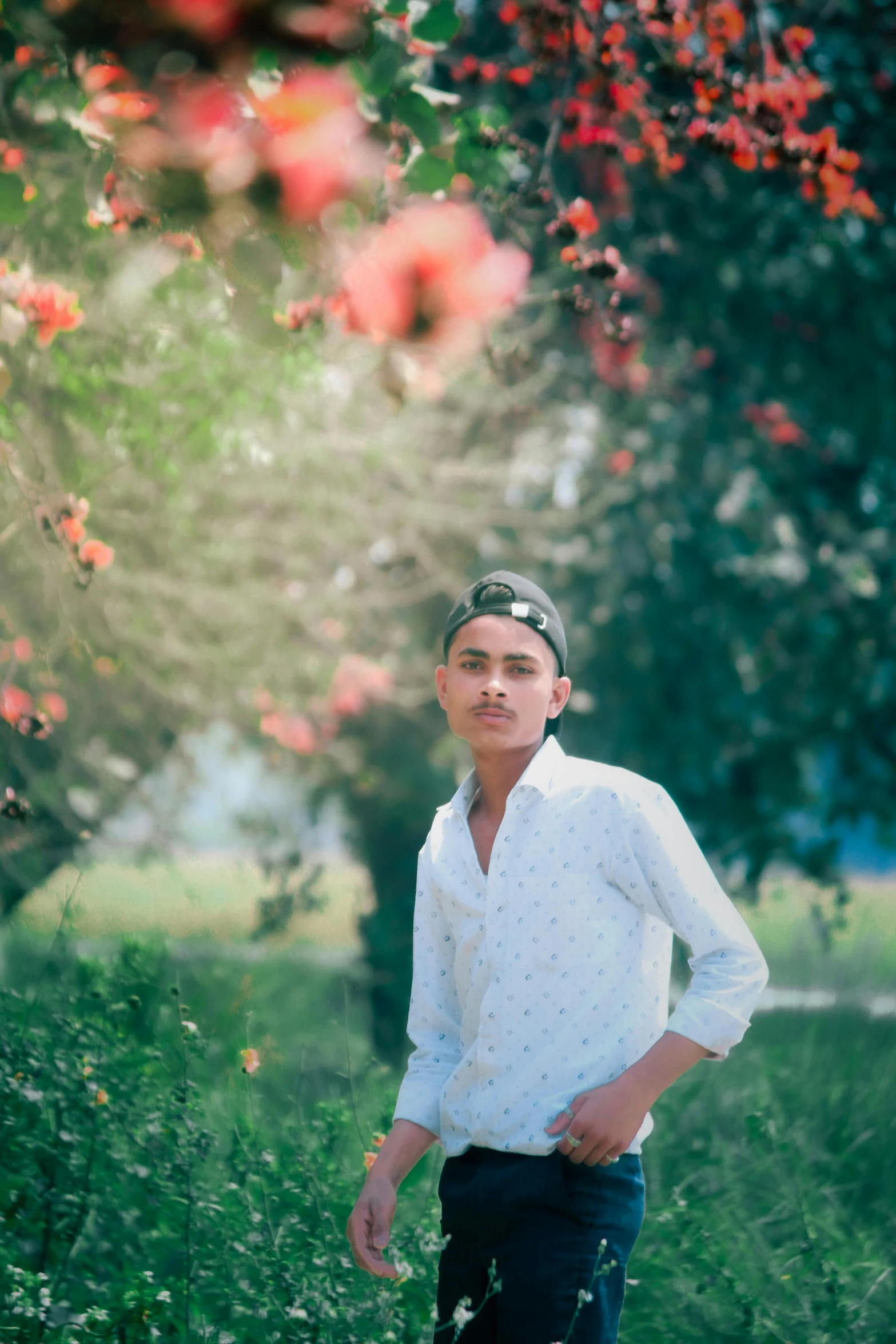 man in white shirt and blue jeans standing next to red flowered tree