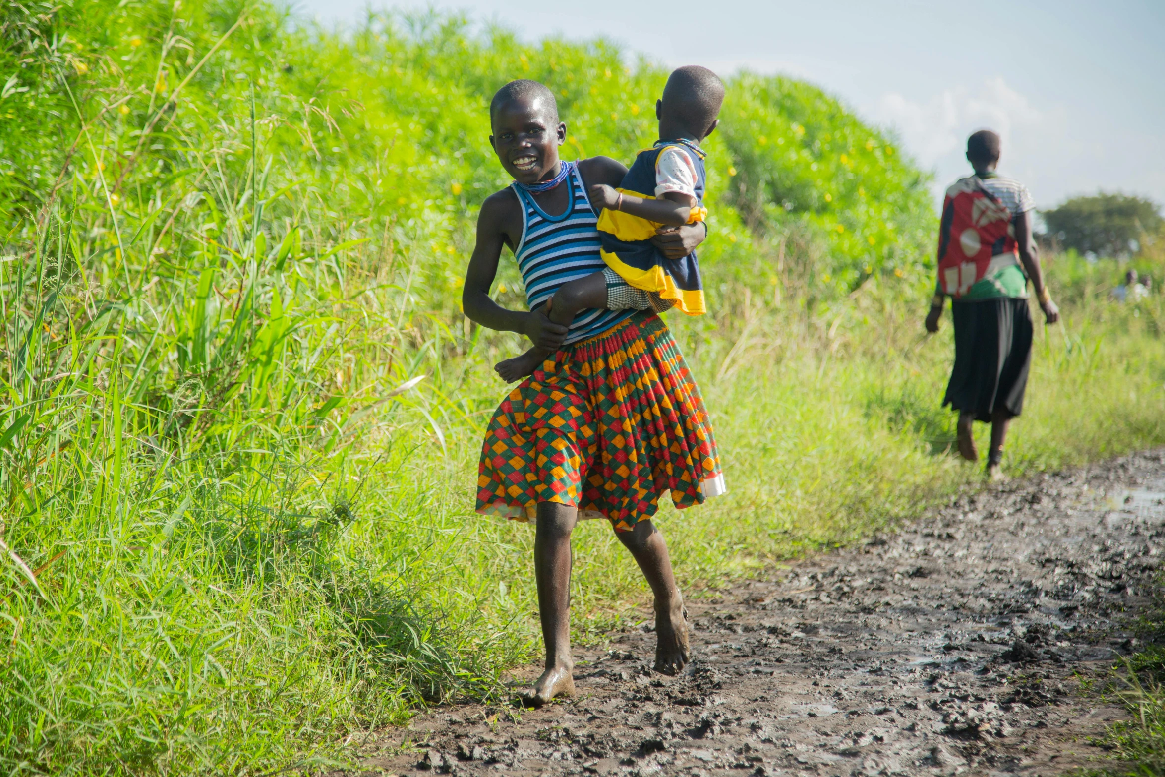 two boys on dirt road carrying infant in arms