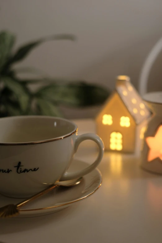 a white tea cup sitting next to a lit house