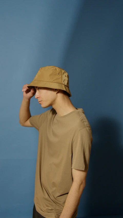 a man standing against a wall holding his hat to his head