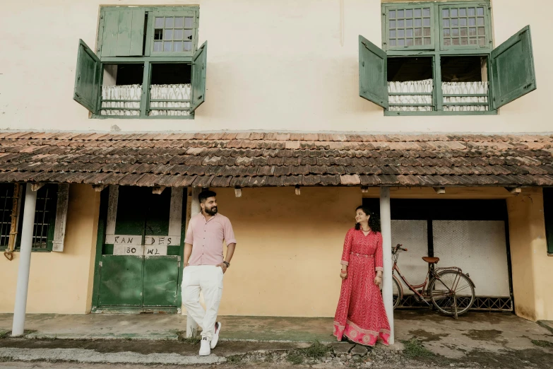 an engaged couple poses in front of a thatched - roofed building with bicycle