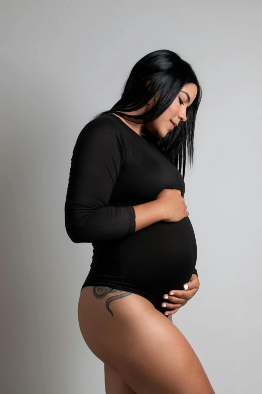 a woman in a tight black dress standing and holding her pregnant belly