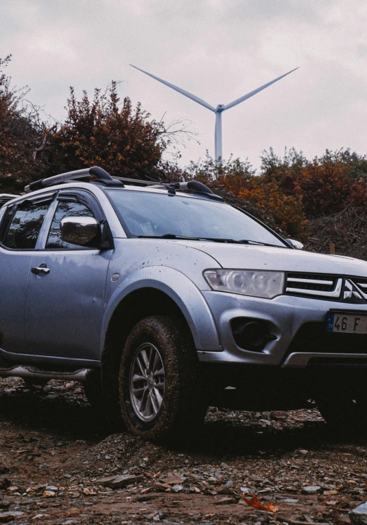 the silver utility truck is parked in the dirt with a wind turbine behind it