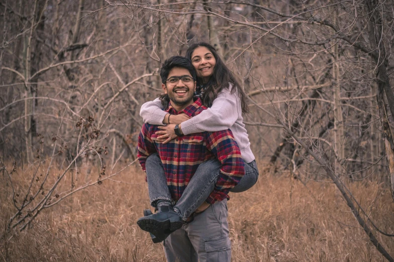 a man is holding his girlfriend and smiling in the woods