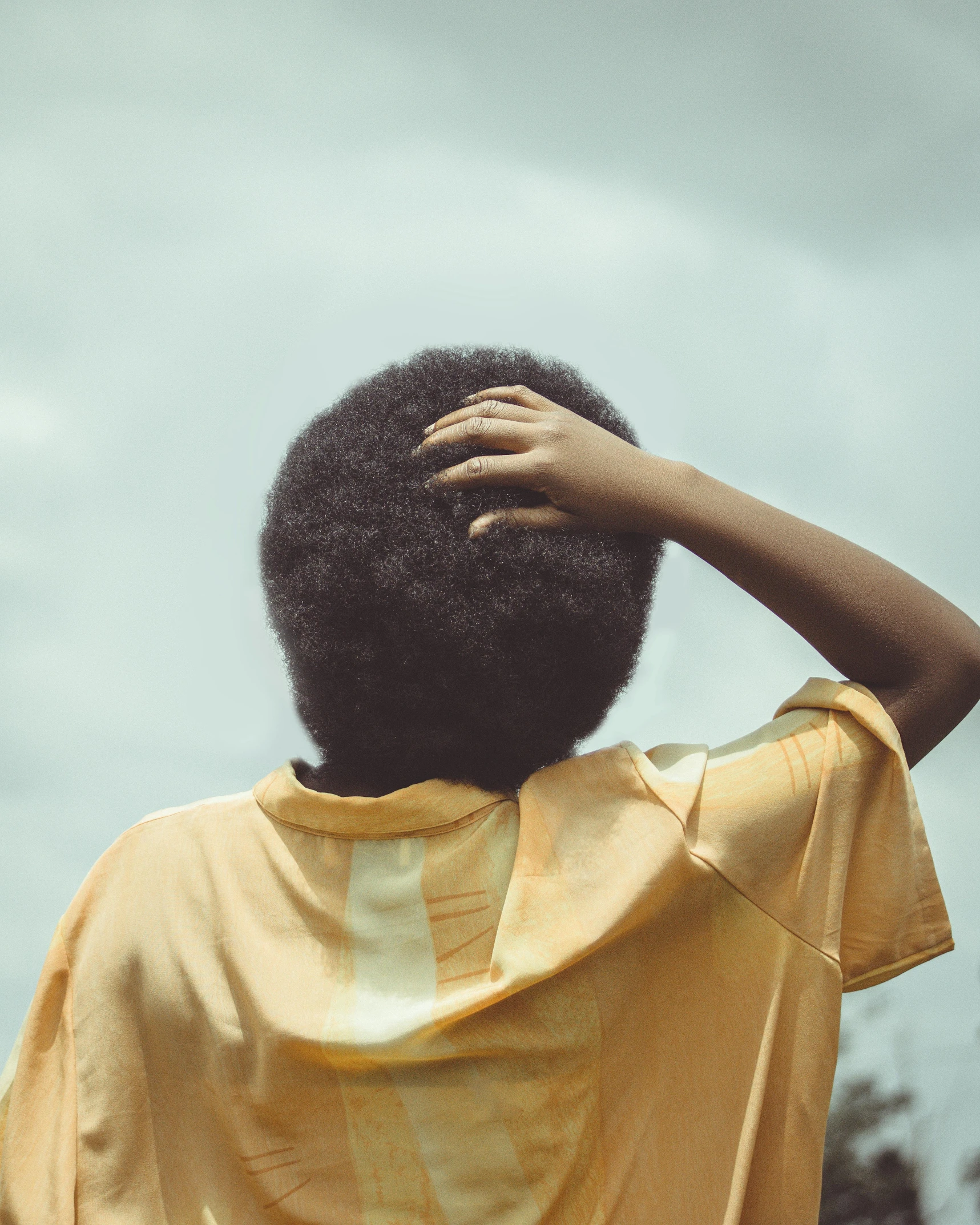 a person wearing a yellow t - shirt is standing with their hand behind their head