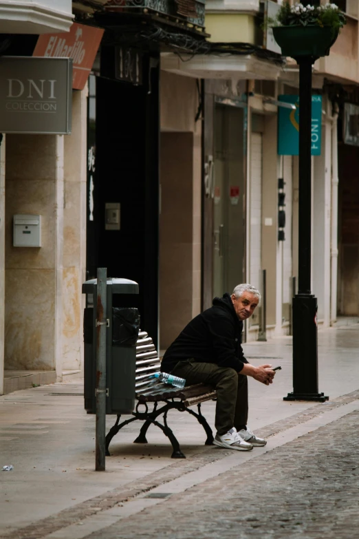 a man sitting on top of a wooden bench in front of a building