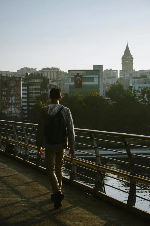 a young man walks across a bridge with some city in the background