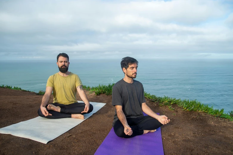 two men sitting on mats, in front of the ocean