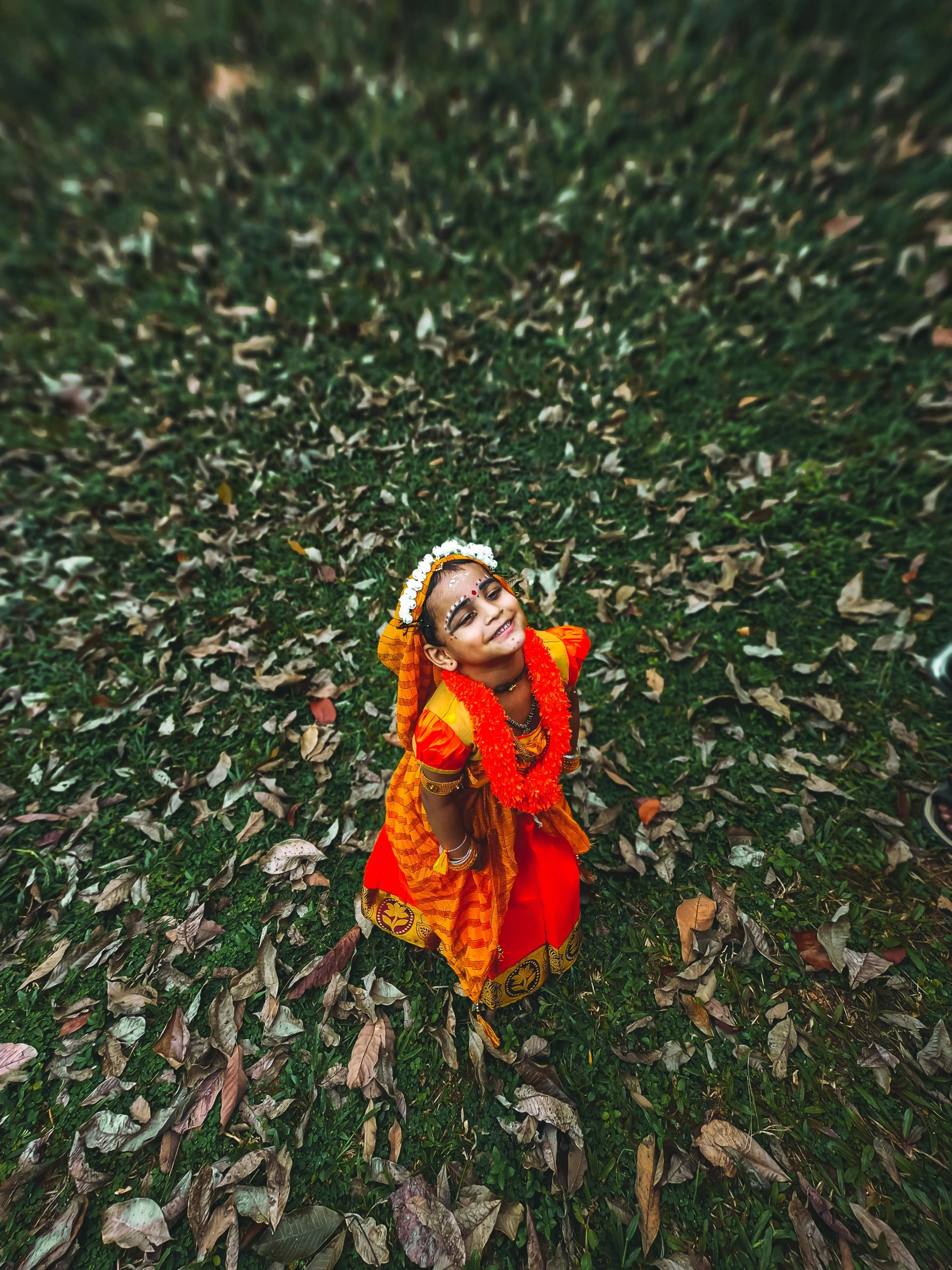a  dressed in orange with red outfit sitting in grass