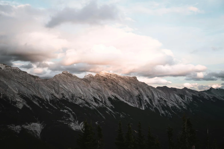 a snowy mountain range with trees and clouds on it