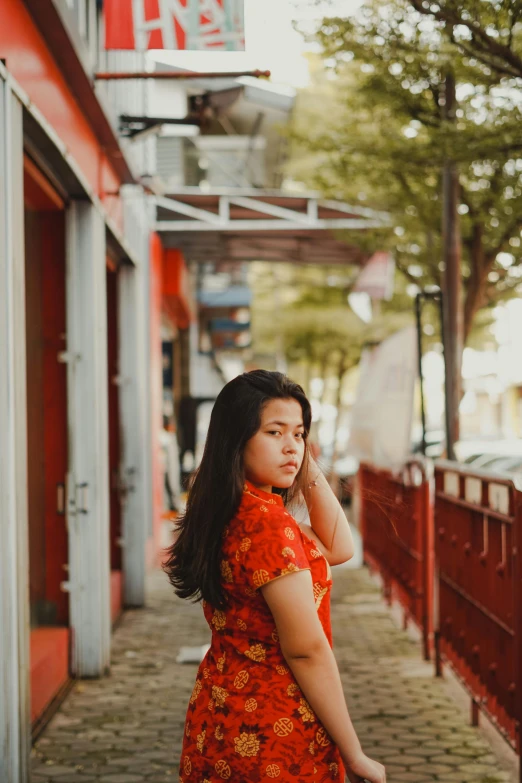 woman in orange dress leaning on a building while listening to cell phone