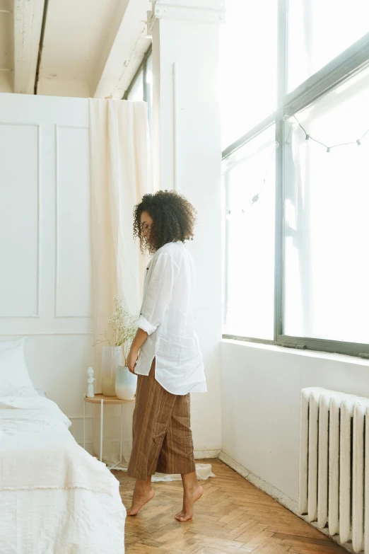 a woman is walking towards a window in a bedroom