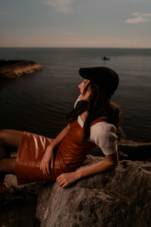 a girl sitting on top of a rock with the water in the background