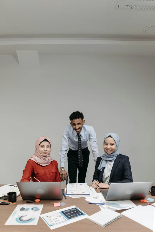 three businesspeople sitting around a table in front of their laptops