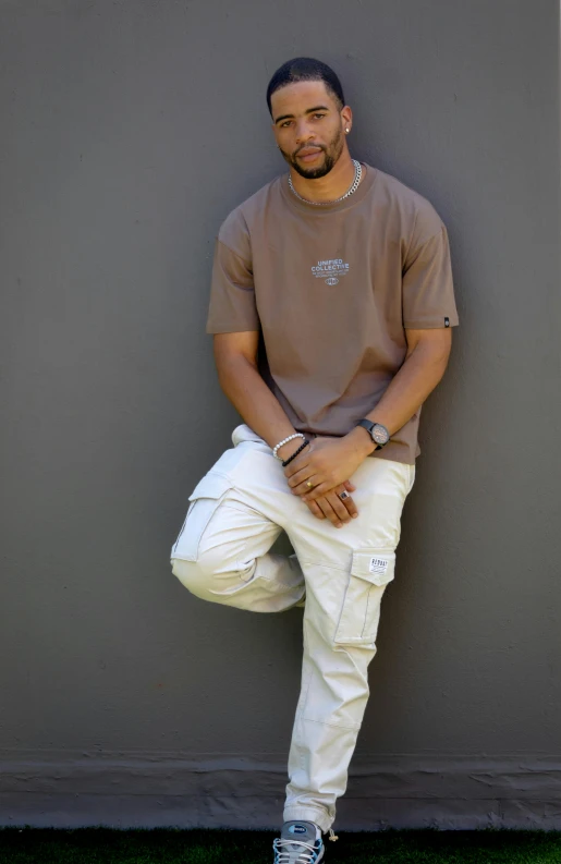 a man wearing all white pants leaning against a wall