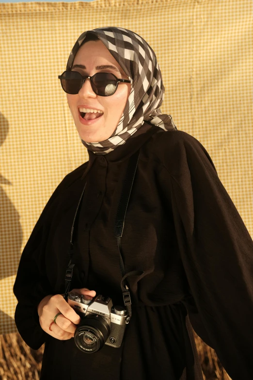 a woman wearing a black dress and black sunglasses holding a camera