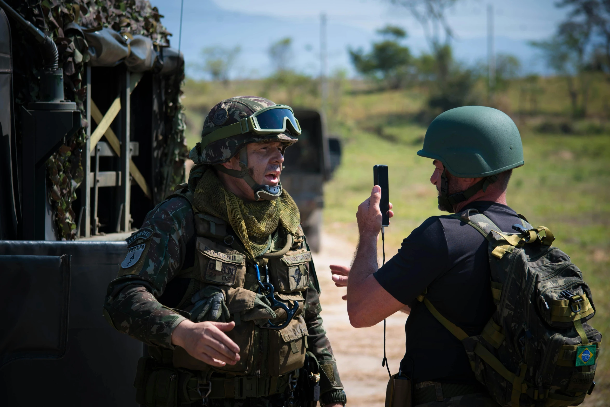 two soldiers standing in front of a truck taking a selfie with a phone